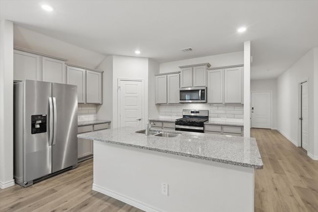 Kitchen with appliances with stainless steel finishes, gray cabinets, decorative backsplash, light wood-style flooring, and recessed lighting | Image 15