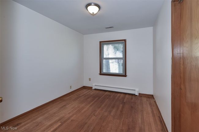 Unfurnished room with a baseboard radiator, visible vents, baseboards, and dark wood-style flooring | Image 31
