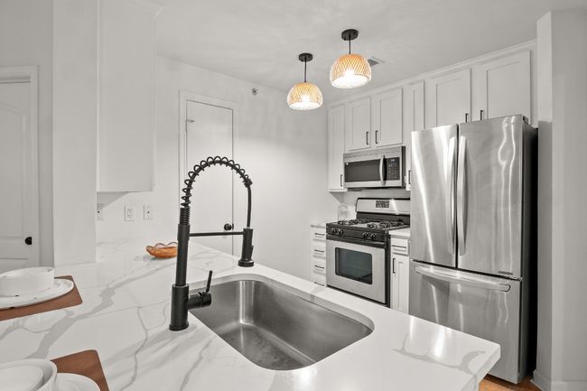 Kitchen featuring appliances with stainless steel finishes, a sink, white cabinetry, and decorative light fixtures | Image 6