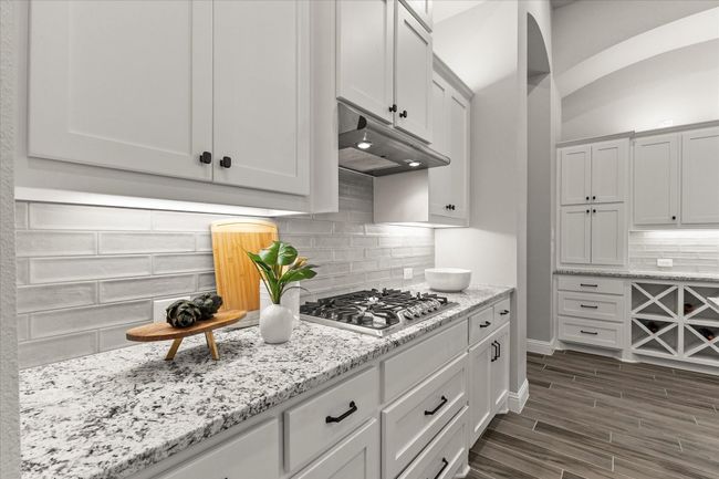 Kitchen with under cabinet range hood, stainless steel gas stovetop, decorative backsplash, light stone granite countertops, and dark wood finished floors | Image 18