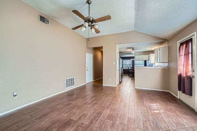 Unfurnished living room with vaulted ceiling, ceiling fan, a textured ceiling, and wood finished floors | Image 7