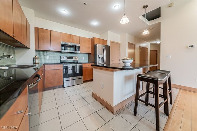 Kitchen with stainless steel appliances, tasteful backsplash, a kitchen breakfast bar, dark countertops, and pendant lights. | Image 16