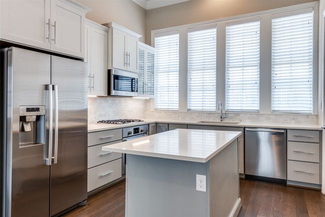 Kitchen featuring stainless steel appliances, dark wood-type flooring, tasteful backsplash, a kitchen island, and ornamental molding | Image 16