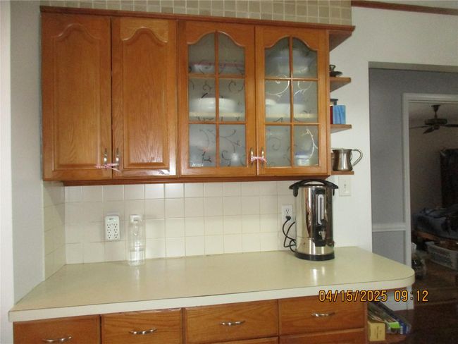 Kitchen featuring glass insert cabinets, ceiling fan, light countertops, brown cabinetry, and backsplash | Image 6