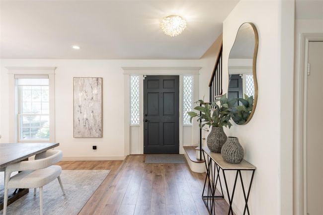 This inviting entryway features a stylish black front door framed by decorative windows. The space is bright with natural light, showcasing a modern interior with wooden floors. | Image 5