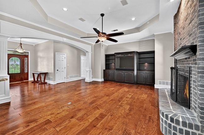 Unfurnished living room with a raised ceiling, a ceiling fan, arched walkways, ornate columns, and crown molding | Image 9