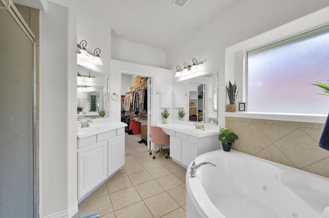 The primary suite bathroom boasts split vanities, a jetted tub, separate shower, an oversized walk-in closet, and a thoughtfully designed ledge perfectly positioned for a TV or decor. | Image 21