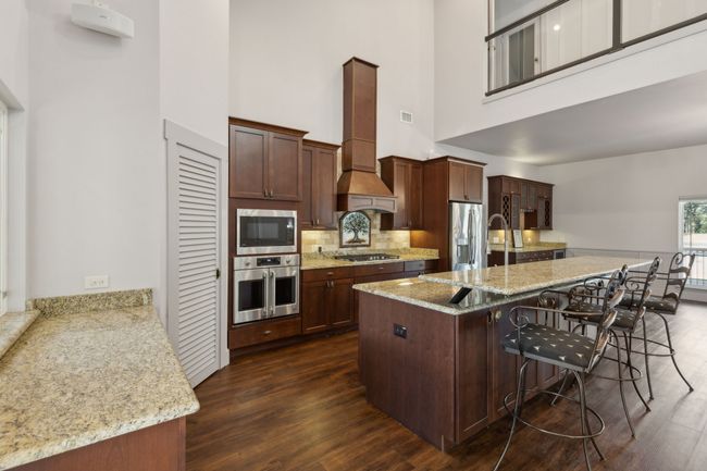 Kitchen featuring a kitchen bar, appliances with stainless steel finishes, dark wood-type flooring, and premium range hood | Image 7