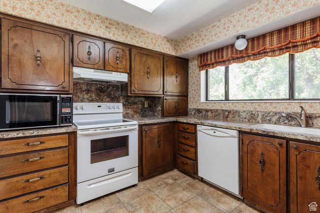 Kitchen with white appliances, under cabinet range hood, light tile patterned floors, backsplash, and light countertops | Image 8