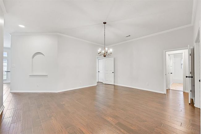 An oversized dining room offers the perfect setting for large gatherings, featuring warm engineered wood floors, crisp crown molding, a classic chandelier, and a built-in arched wall niche for added charm and display. | Image 6