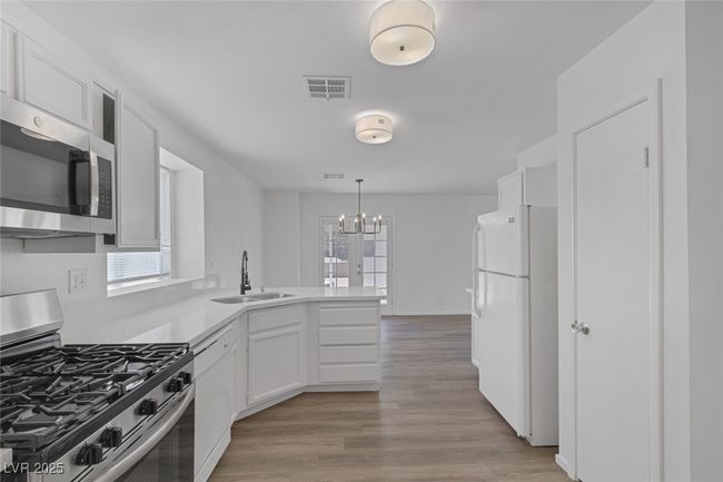 Kitchen with stainless steel appliances, a peninsula, white cabinetry, a chandelier, and light countertops | Image 12
