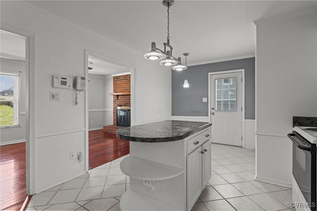 Kitchen with white cabinets, light tile patterned flooring, crown molding, electric range oven, and a brick fireplace | Image 14