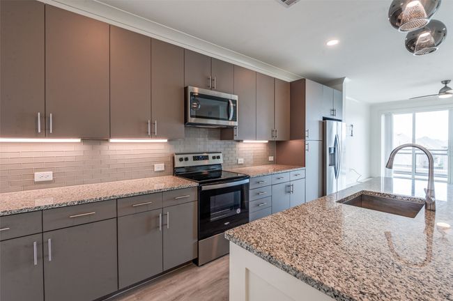 Kitchen featuring stainless steel appliances, light wood finished floors, backsplash, light stone counters, and ceiling fan | Image 11