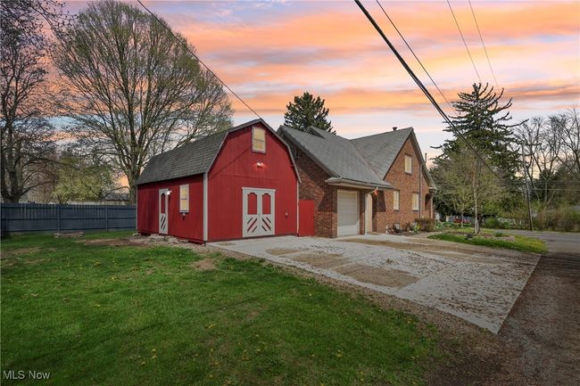 Outdoor structure at dusk featuring concrete driveway, fence, an outbuilding, a yard, and a barn | Image 45