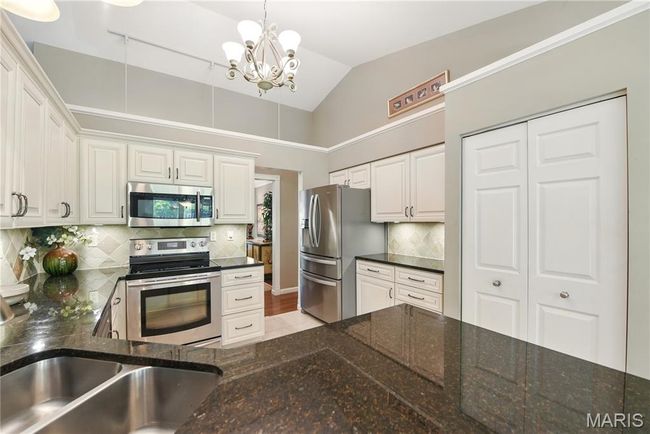 Kitchen featuring stainless steel appliances, a chandelier, white cabinets, backsplash, and vaulted ceiling | Image 9
