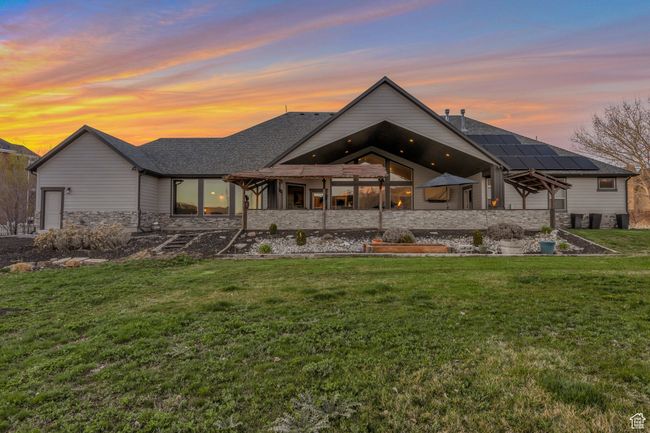 Back of house at dusk featuring a shingled roof, stone siding, a lawn, and roof mounted solar panels | Image 36