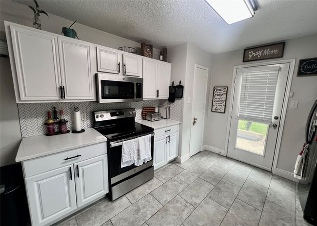 Kitchen featuring appliances with stainless steel finishes, a textured ceiling, backsplash, white cabinetry, and light countertops | Image 8