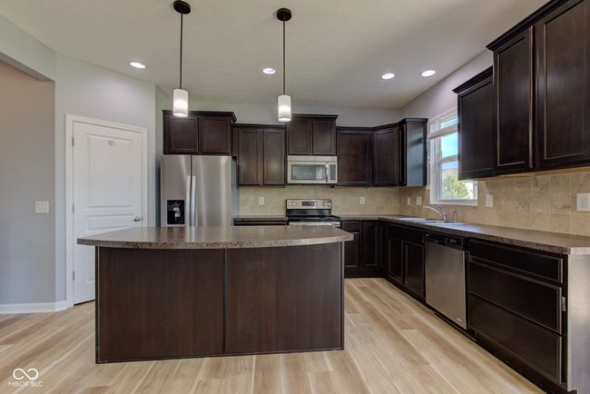 kitchen featuring appliances with stainless steel finishes, light wood-style floors, dark brown cabinetry, a center island, and recessed lighting | Image 11