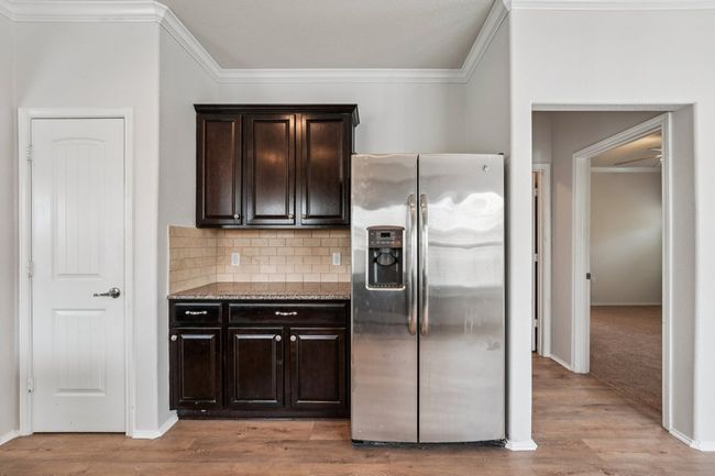 Kitchen featuring stainless steel fridge with ice dispenser, dark brown cabinetry, ornamental molding, decorative backsplash, and light wood-type flooring | Image 15