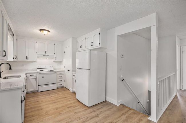 Kitchen featuring white appliances, under cabinet range hood, a sink, white cabinets, and a textured ceiling | Image 7