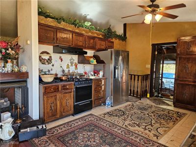 Kitchen with black stove, vaulted ceiling, stainless steel fridge with ice dispenser, light tile patterned floors, and ceiling fan | Image 2