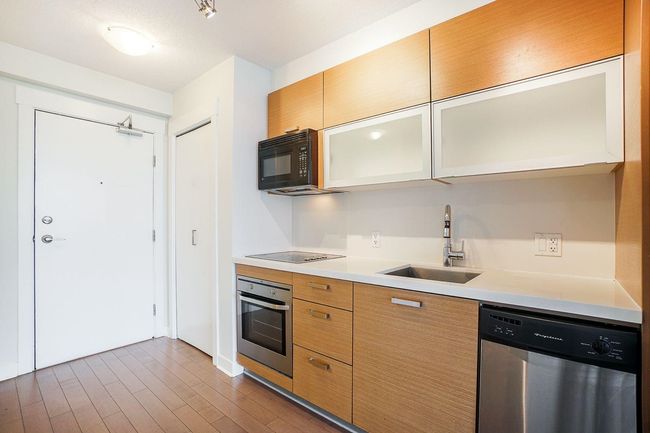 Kitchen featuring glass insert cabinets, a sink, light countertops, black appliances, and dark wood-style flooring | Image 5