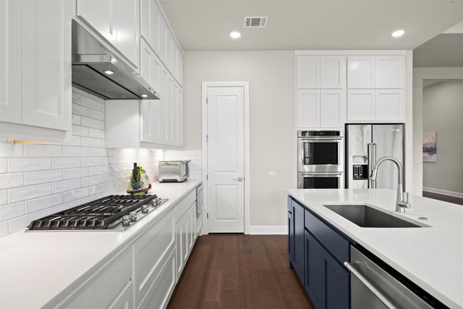Kitchen featuring range hood, stainless steel appliances, white cabinets, light countertops, and dark wood finished floors | Image 18