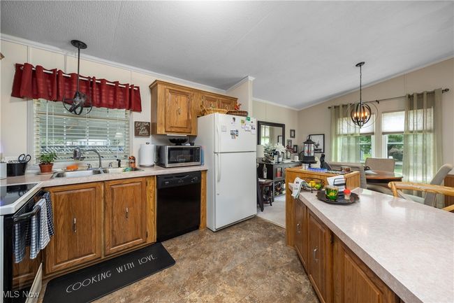 Kitchen featuring dishwasher, freestanding refrigerator, stainless steel microwave, range with electric stovetop, and brown cabinetry | Image 27