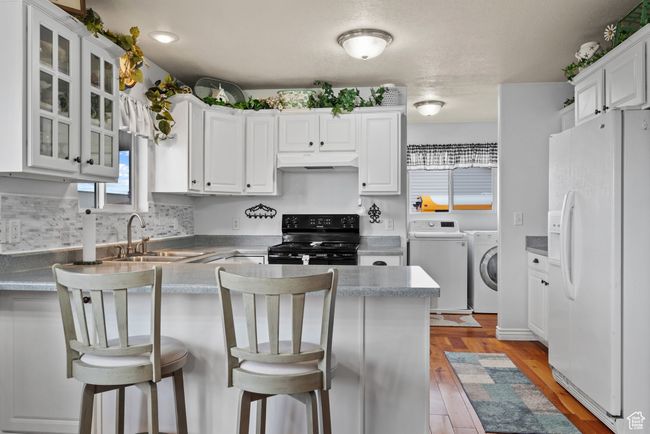 Kitchen featuring a sink, washing machine and clothes dryer, white fridge with ice dispenser, a peninsula, and black range oven | Image 8