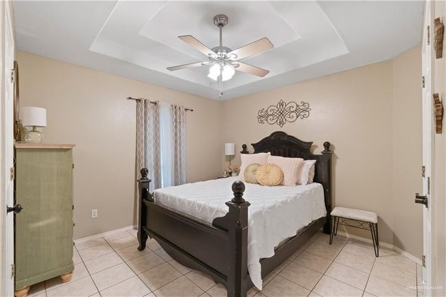 Bedroom with a raised ceiling, light tile patterned floors, and a ceiling fan | Image 6