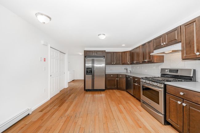 Kitchen with tasteful backsplash, a baseboard heating unit, light wood-type flooring, under cabinet range hood, and appliances with stainless steel finishes | Image 7