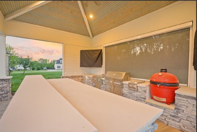 This luxury outdoor kitchen features built-in appliances, side burners, a griddle, fridge, and a Kamado Joe smoker—plus a spacious bar top and stone finishes, perfect for entertaining in style! | Image 6