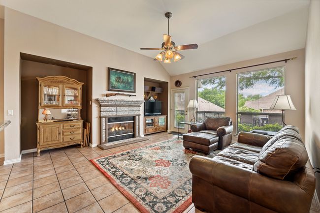 Living area featuring vaulted ceiling, built in shelves, a tile fireplace, ceiling fan, and light tile patterned floors | Image 12