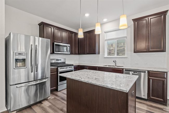 Kitchen featuring pendant lighting, appliances with stainless steel finishes, dark brown cabinetry, a kitchen island, and sink | Image 18