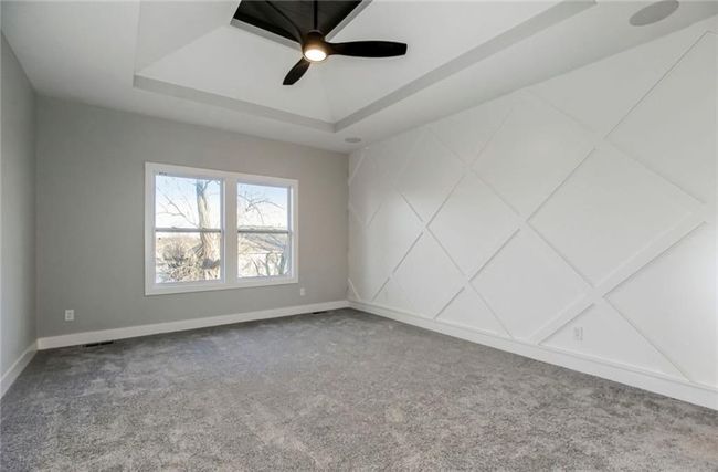 Carpeted empty room featuring a raised ceiling, baseboards, and ceiling fan | Image 9