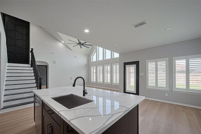Spacious living area features high ceilings, large windows, and modern finishes. It includes a sleek kitchen island with a marble countertop, an elegant staircase, and abundant natural light. | Image 13