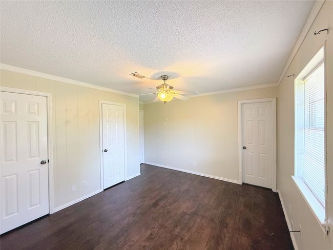 Unfurnished bedroom with a textured ceiling, dark wood-style floors, crown molding, and ceiling fan | Image 12