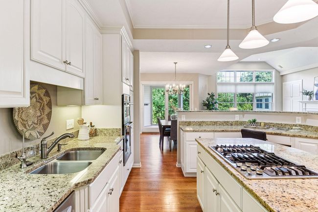 Open kitchen design with ample storage, professional-grade gas cooktop, and warm hardwood flooring. | Image 13