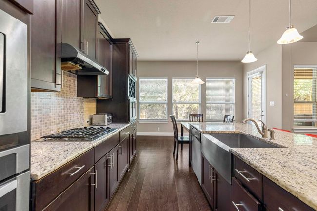 Kitchen with under cabinet range hood, tasteful backsplash, dark wood-style floors, stainless steel appliances, and light stone countertops | Image 14