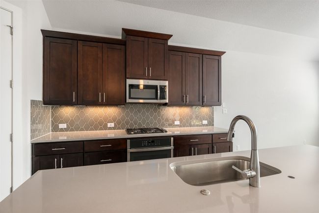 Kitchen with stainless steel appliances, tasteful backsplash, dark brown cabinetry, and light countertops | Image 12