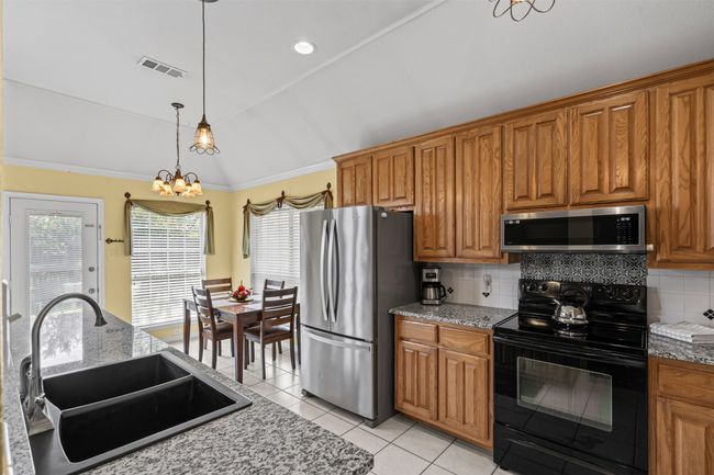 Kitchen with appliances with stainless steel finishes, a sink, tasteful backsplash, brown cabinets, and lofted ceiling | Image 11