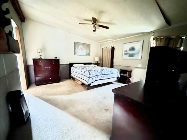 This photo shows a cozy bedroom with a double bed, ceiling fan, and two dressers. The room is carpeted and has soft, neutral walls with framed artwork, offering a warm and inviting atmosphere. | Image 6