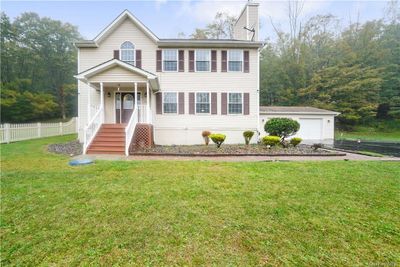 Colonial-style home with a covered front porch and paved walkway leading to the driveway. | Image 1