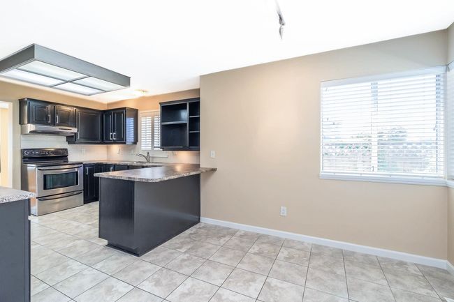 Kitchen with a peninsula, baseboards, under cabinet range hood, and stainless steel electric stove | Image 13