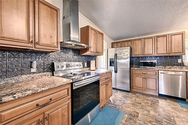 Kitchen with appliances with stainless steel finishes, wall chimney exhaust hood, a textured ceiling, light stone countertops, and brown cabinets | Image 4