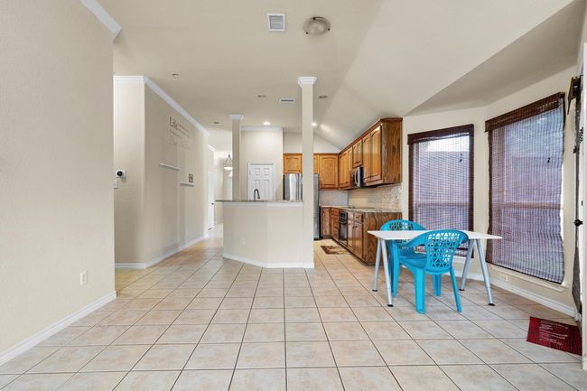 Kitchen with appliances with stainless steel finishes, light tile patterned flooring, brown cabinetry, decorative backsplash, and lofted ceiling | Image 11