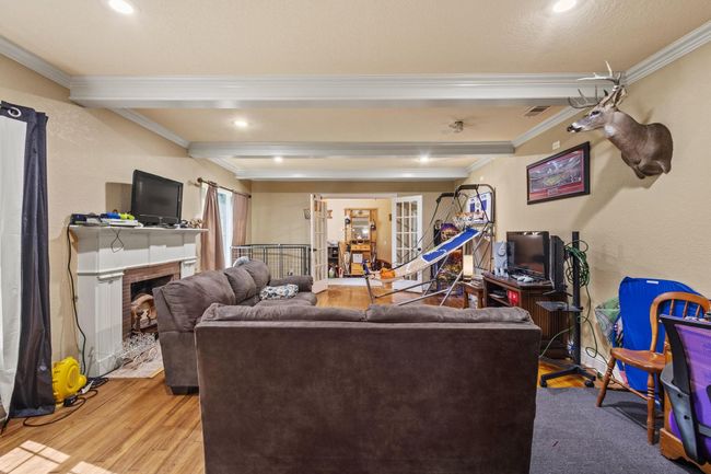 Living area featuring wood finished floors, visible vents, ornamental molding, beam ceiling, and a fireplace | Image 14