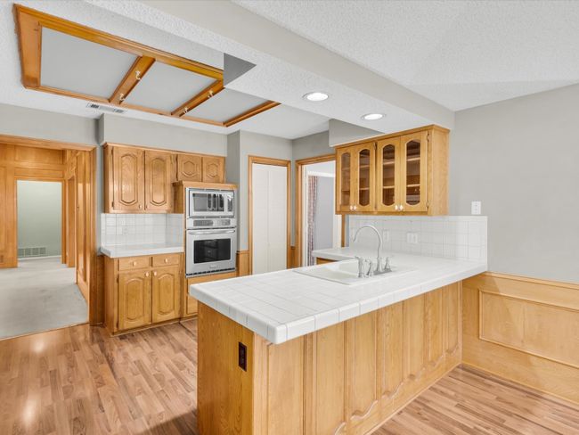 Kitchen featuring laminate flooring, wood cabinets, tile counters and peninsula. | Image 16