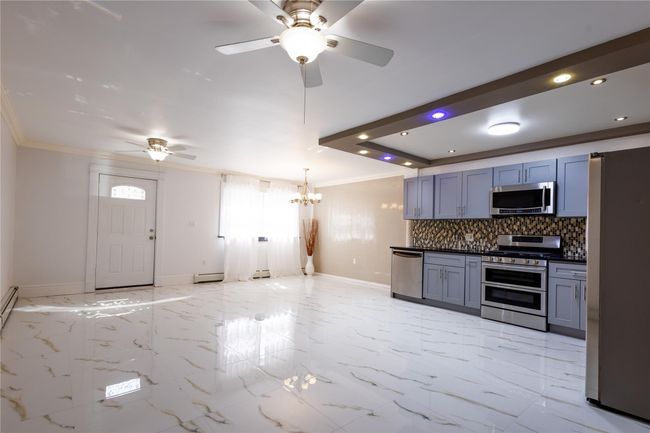 Living room, kitchen, and dining room with backsplash, baseboards, stainless steel appliances, and ceiling fan with notable chandelier | Image 5