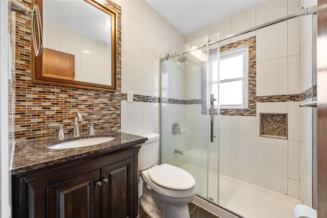 Full bath with decorative backsplash, tile walls, toilet, vanity, and a stall shower | Image 9
